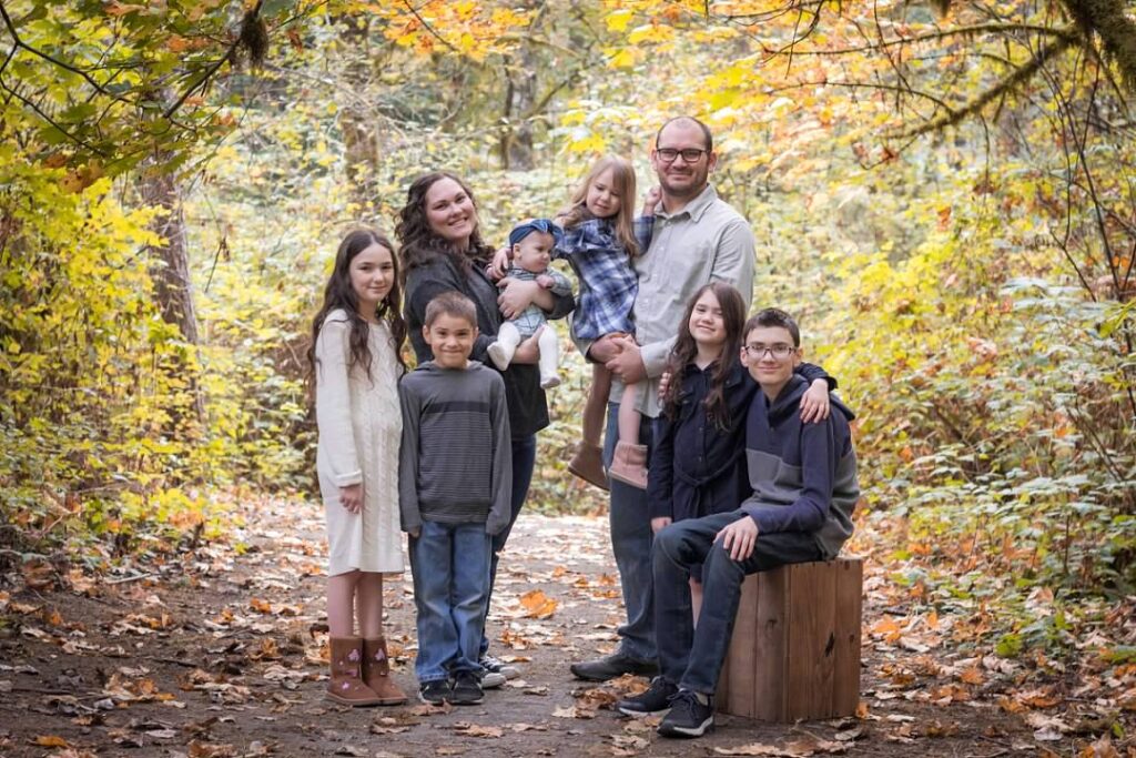 a family of eight smiling and posing for a photo in the forest on a fall day