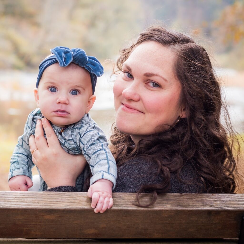 a woman holding her baby girl on a bench in the forest on a fall day