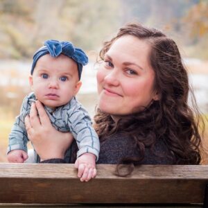 a woman holding her baby girl on a bench in the forest on a fall day